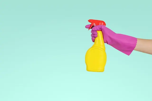 Hand wearing a purple glove holding a yellow spray bottle.