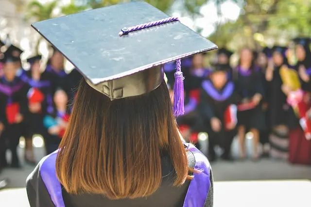 Graduate in cap and gown facing a crowd of fellow graduates.